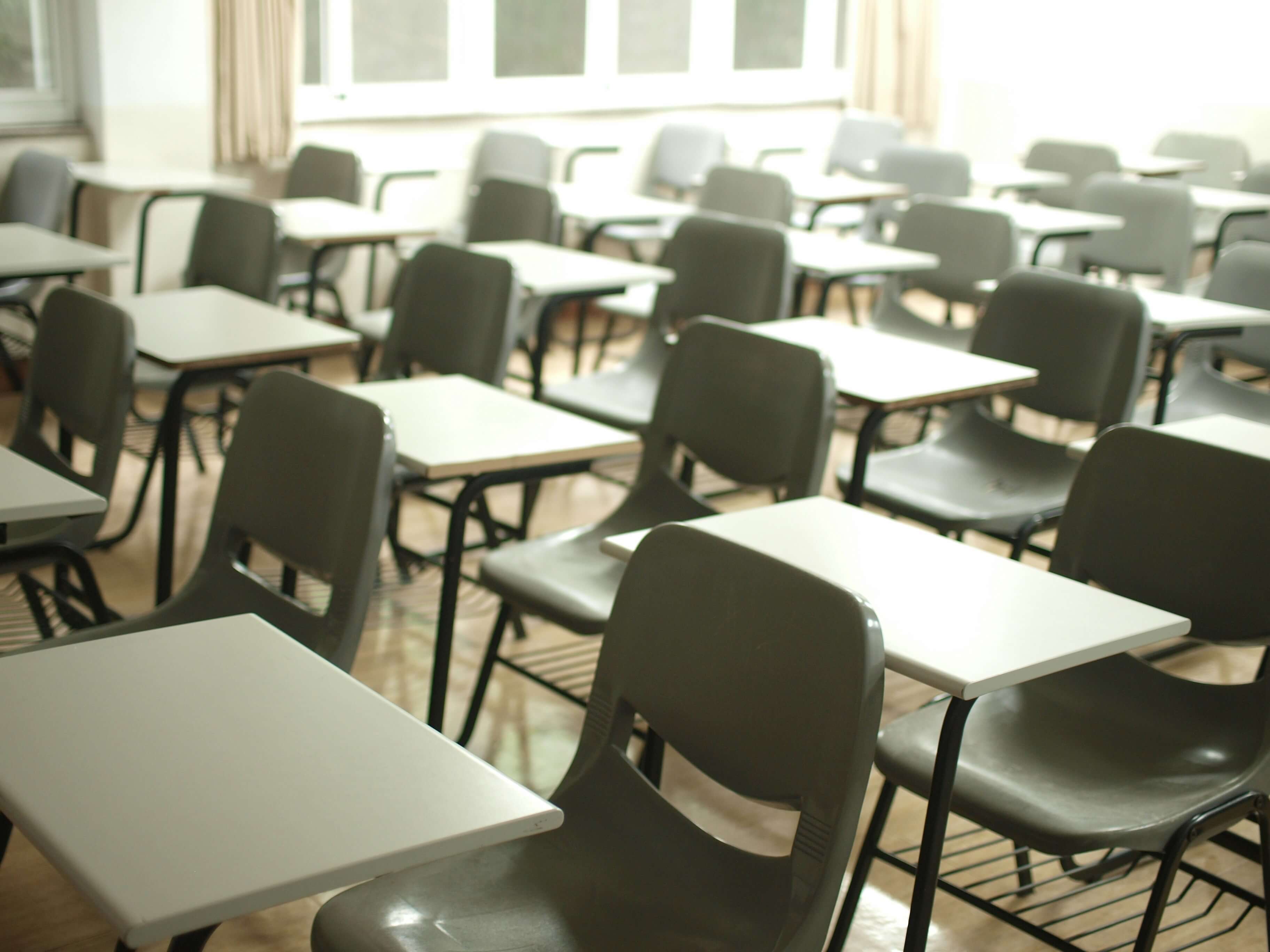 A class room that is full of seats with desks attached to them.