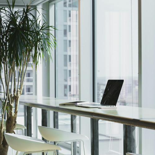 Computer on desk over looking a wall of glass that is above a city.